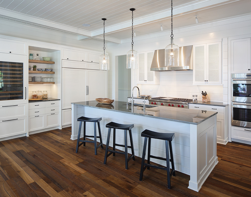 Country l-shaped kitchen in Milwaukee with a double-bowl sink, recessed-panel cabinets, white cabinets, white splashback, timber splashback, medium hardwood floors, with island and brown floor.