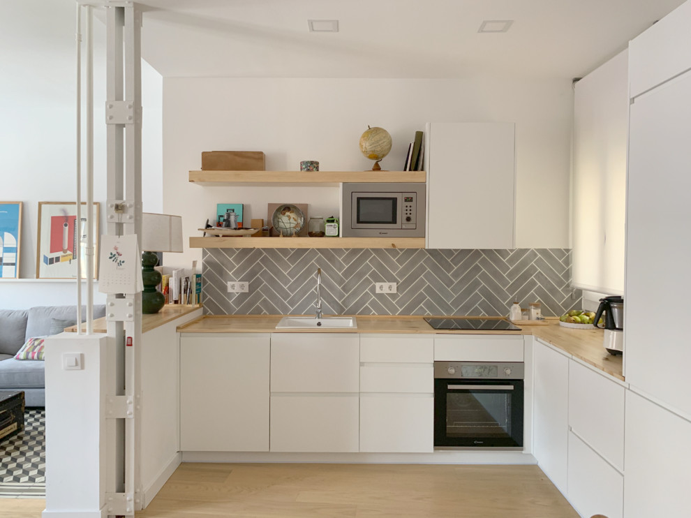 Inspiration for a small contemporary l-shaped open plan kitchen in Madrid with a drop-in sink, flat-panel cabinets, white cabinets, wood benchtops, grey splashback, stainless steel appliances, light hardwood floors, ceramic splashback, brown floor and brown benchtop.