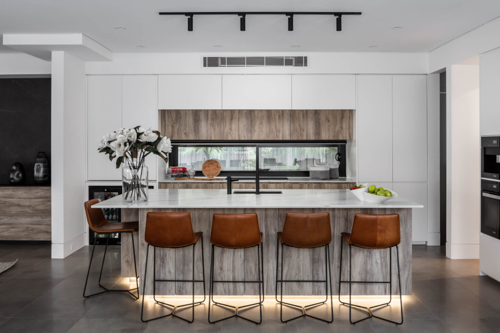 This is an example of a contemporary l-shaped kitchen in Sydney with flat-panel cabinets, white cabinets, window splashback, with island, grey floor and white benchtop.