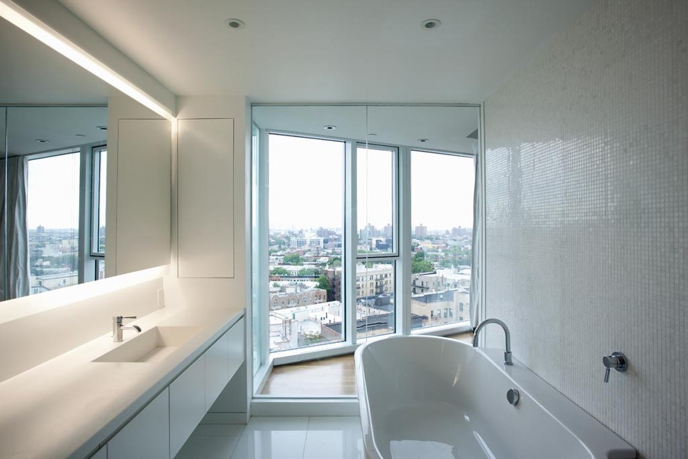 Contemporary bathroom in New York with an integrated sink, flat-panel cabinets, white cabinets, a freestanding tub and white tile.