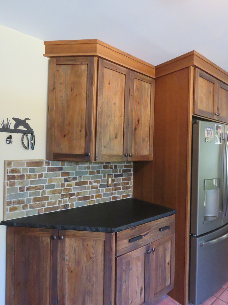 This is an example of a mid-sized country u-shaped eat-in kitchen in Philadelphia with an undermount sink, shaker cabinets, distressed cabinets, granite benchtops, multi-coloured splashback, brick splashback, stainless steel appliances, terra-cotta floors, with island and red floor.