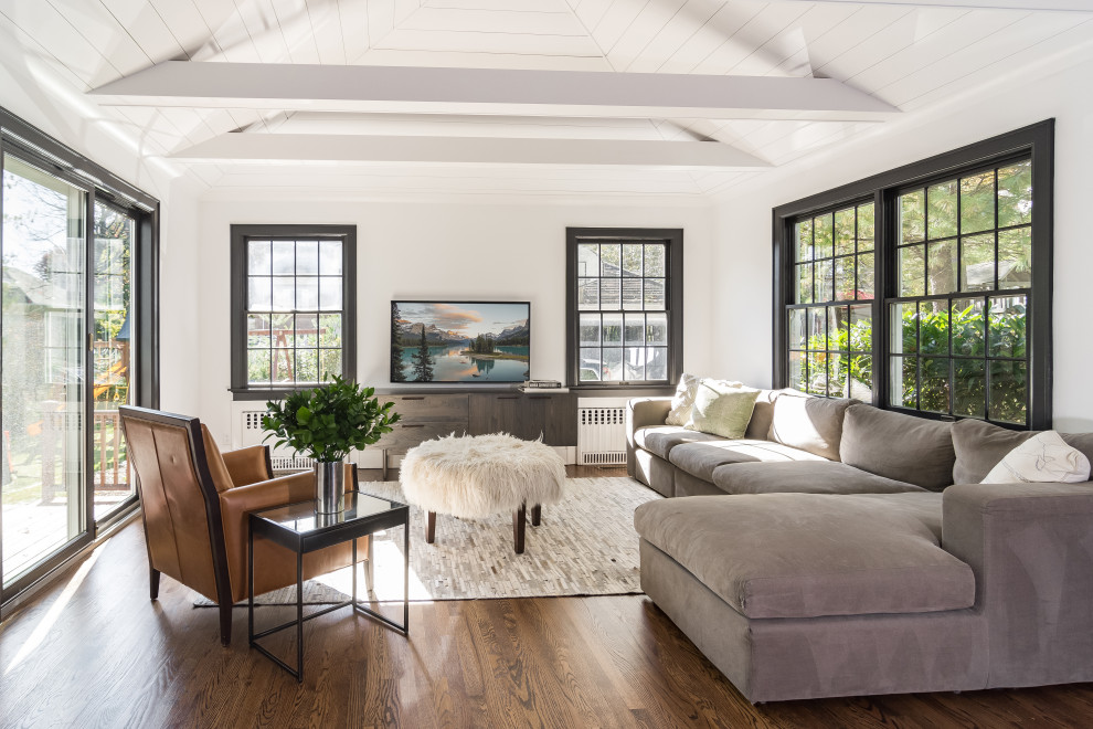 Mid-sized transitional open concept family room in New York with white walls, medium hardwood floors, no fireplace, brown floor, a wall-mounted tv and vaulted.