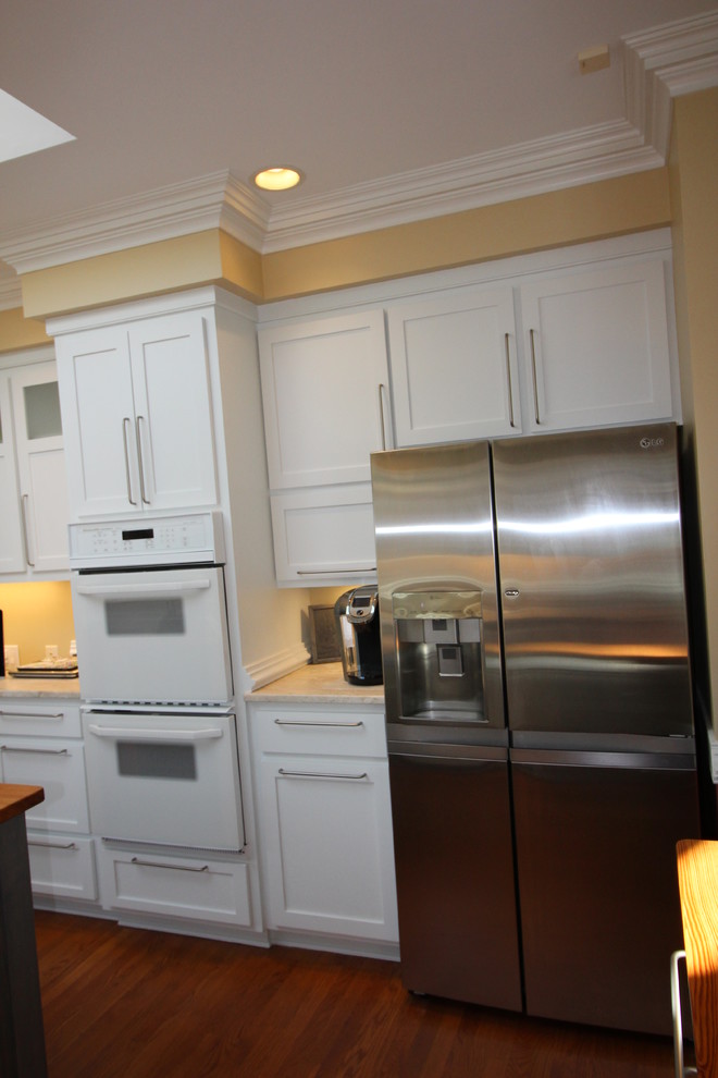 Inspiration for a mid-sized transitional u-shaped medium tone wood floor eat-in kitchen remodel with a farmhouse sink, shaker cabinets, yellow cabinets, marble countertops, beige backsplash, stone tile backsplash, stainless steel appliances and an island