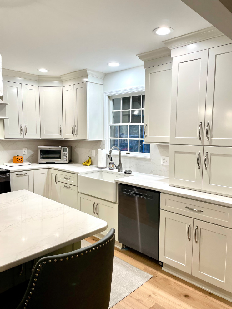 Inspiration for a transitional l-shaped light wood floor and beige floor eat-in kitchen remodel with a farmhouse sink, shaker cabinets, white cabinets, quartz countertops, white backsplash, quartz backsplash, black appliances, an island and white countertops