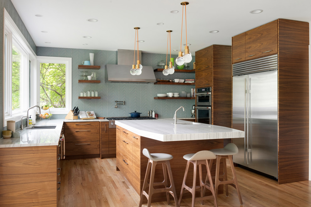 Photo of a midcentury kitchen in Minneapolis with a double-bowl sink, flat-panel cabinets, medium wood cabinets, blue splashback, stainless steel appliances, light hardwood floors, with island and white benchtop.