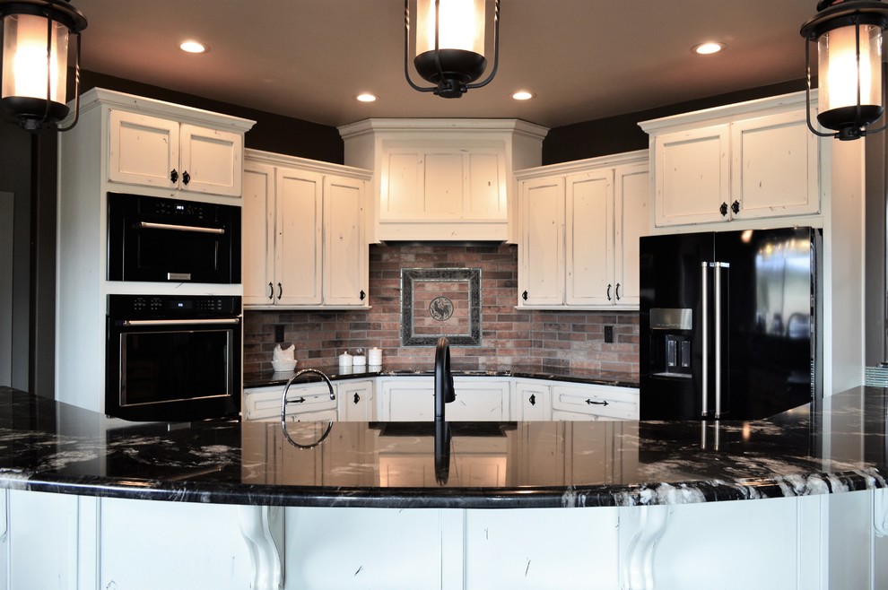 Mid-sized country u-shaped kitchen in Denver with recessed-panel cabinets, distressed cabinets, granite benchtops, red splashback, brick splashback, black appliances and with island.