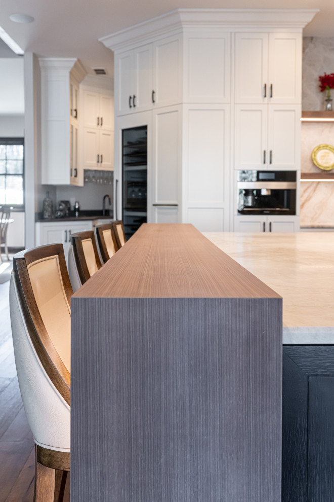 Large transitional medium tone wood floor and brown floor open concept kitchen photo with a double-bowl sink, flat-panel cabinets, white cabinets, quartzite countertops, beige backsplash, stainless steel appliances, an island and beige countertops