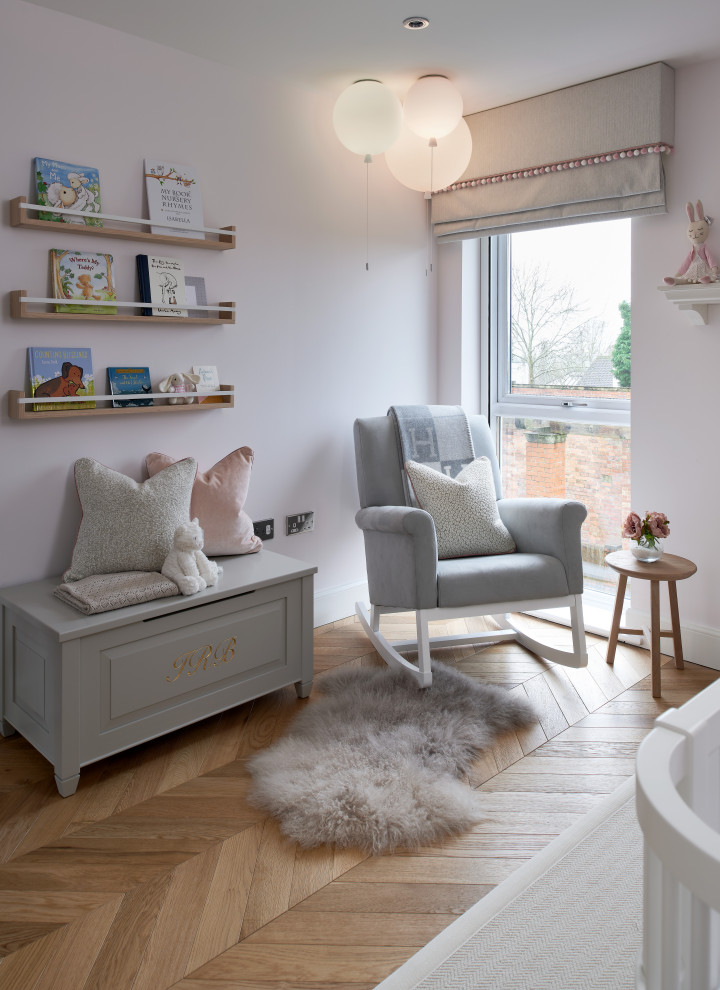 Immagine di una cameretta per neonata minimal di medie dimensioni con pareti rosa, pavimento in legno massello medio e carta da parati