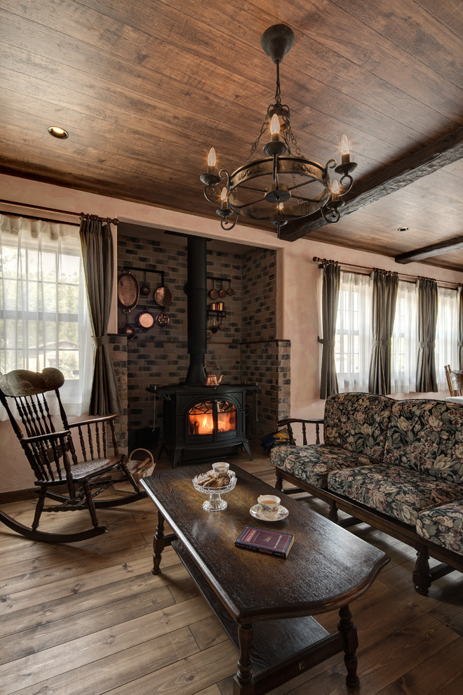 Country living room in Other with pink walls, medium hardwood floors, a wood stove, a brick fireplace surround and brown floor.