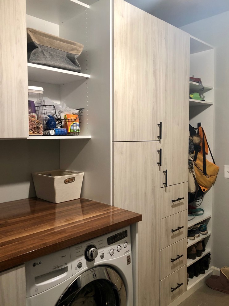 Inspiration for a small transitional galley utility room in Chicago with a drop-in sink, flat-panel cabinets, light wood cabinets, wood benchtops, grey walls, porcelain floors, a side-by-side washer and dryer and grey floor.