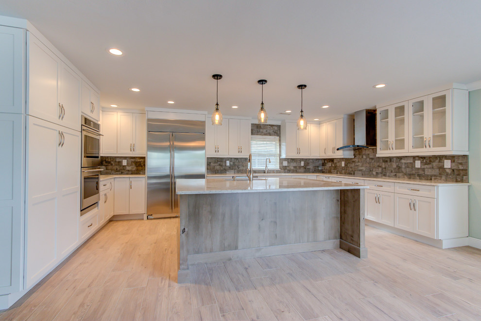 Inspiration for a large transitional u-shaped porcelain tile and brown floor enclosed kitchen remodel with an undermount sink, shaker cabinets, white cabinets, quartz countertops, brown backsplash, stainless steel appliances, an island and beige countertops