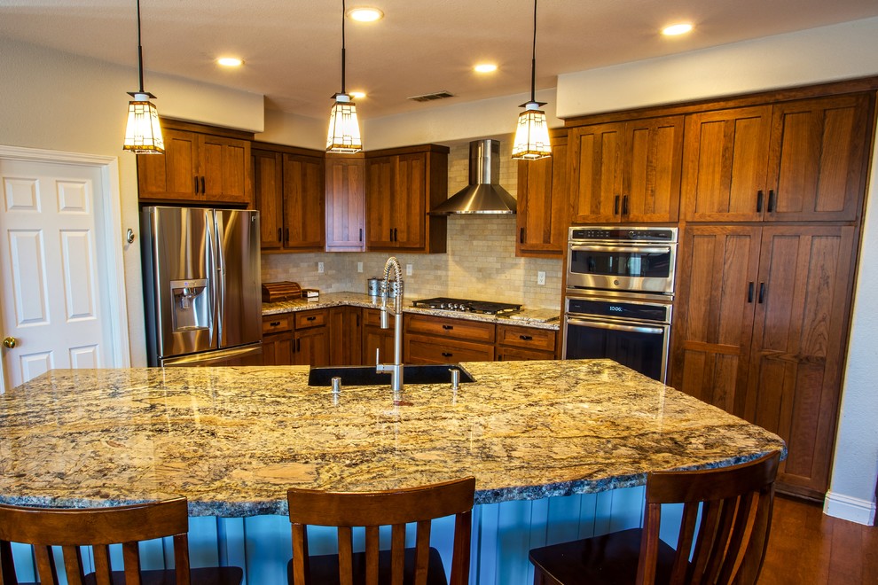Large mountain style dark wood floor and brown floor open concept kitchen photo in Sacramento with a farmhouse sink, shaker cabinets, brown cabinets, granite countertops, beige backsplash, subway tile backsplash, stainless steel appliances, an island and brown countertops