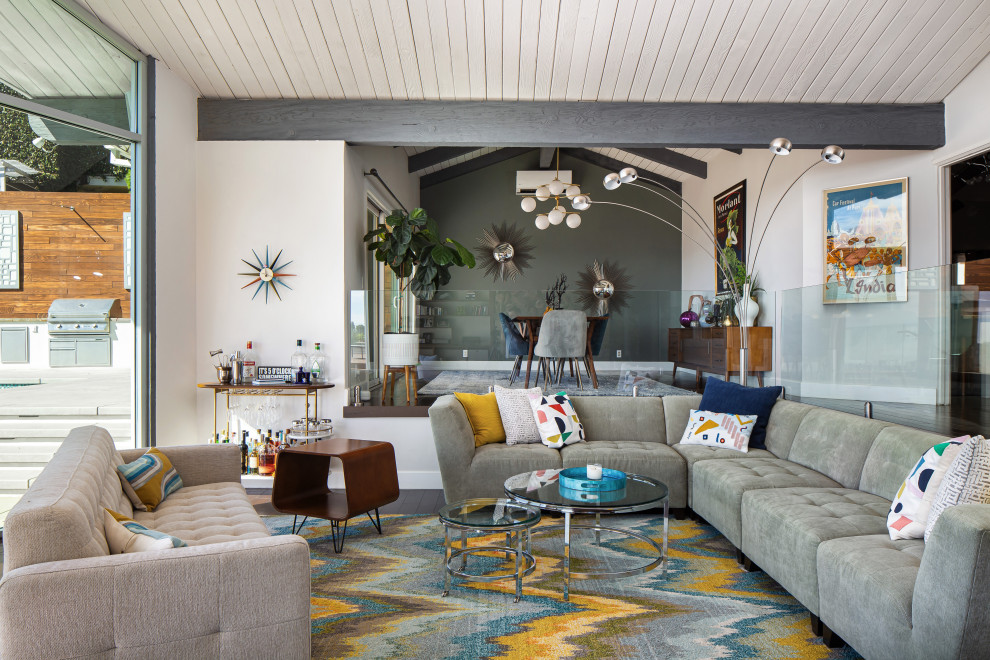 Large midcentury open concept living room in Los Angeles with a home bar, white walls, dark hardwood floors, no tv, brown floor and vaulted.