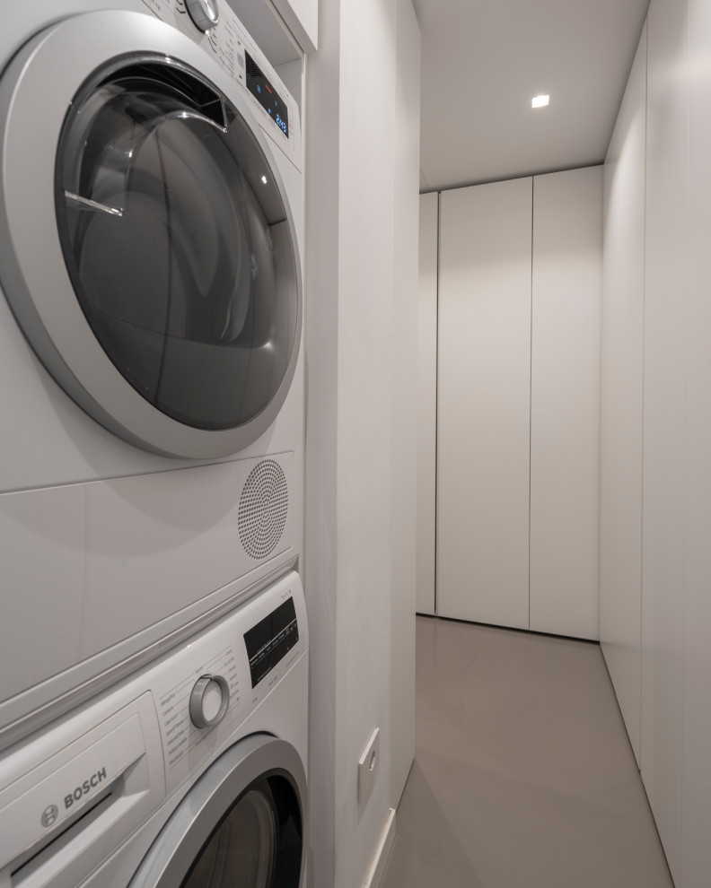 Mid-sized modern u-shaped utility room in Milan with flat-panel cabinets, white cabinets, white walls, a stacked washer and dryer, grey floor and recessed.