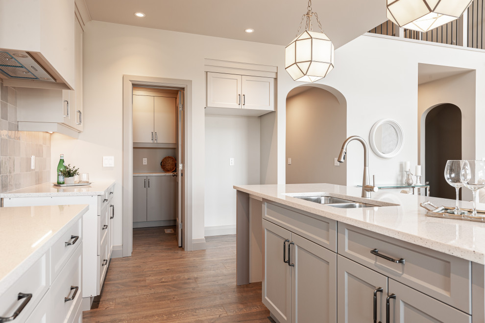 Inspiration for a small transitional galley laminate floor and brown floor open concept kitchen remodel in Toronto with a double-bowl sink, recessed-panel cabinets, beige cabinets, quartz countertops, beige backsplash, porcelain backsplash, stainless steel appliances, an island and white countertops