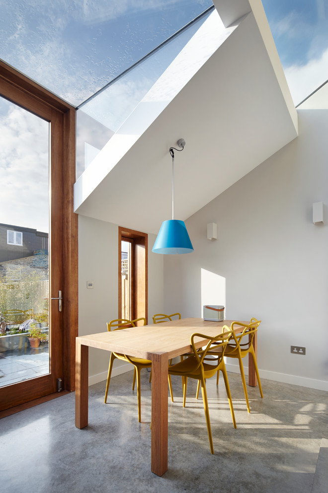 This is an example of a contemporary open plan dining in London with white walls and concrete floors.