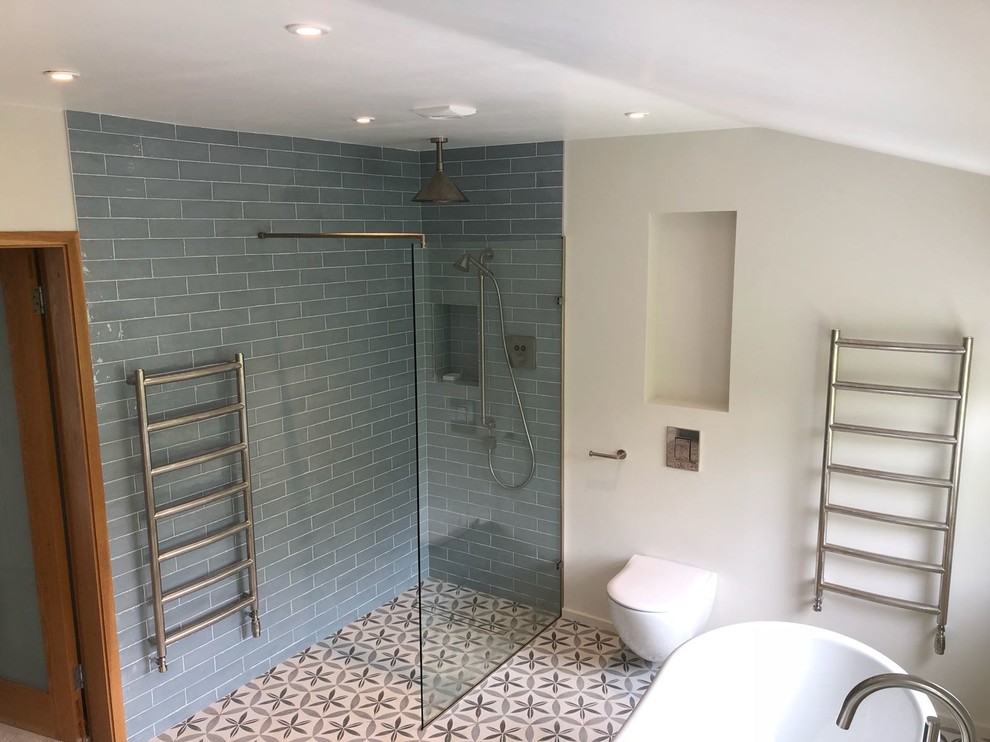 This is an example of a large traditional master bathroom in London with furniture-like cabinets, light wood cabinets, a freestanding tub, an open shower, a wall-mount toilet, gray tile, ceramic tile, ceramic floors, a trough sink and an open shower.