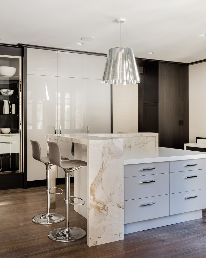 This is an example of a large modern u-shaped open plan kitchen in Boston with marble benchtops, stone slab splashback, multiple islands, white benchtop, an undermount sink, brown floor, black appliances, white splashback and medium hardwood floors.