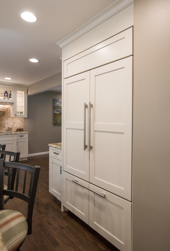 Inspiration for a large transitional u-shaped medium tone wood floor and brown floor eat-in kitchen remodel with an undermount sink, shaker cabinets, white cabinets, granite countertops, beige backsplash, travertine backsplash, paneled appliances and an island