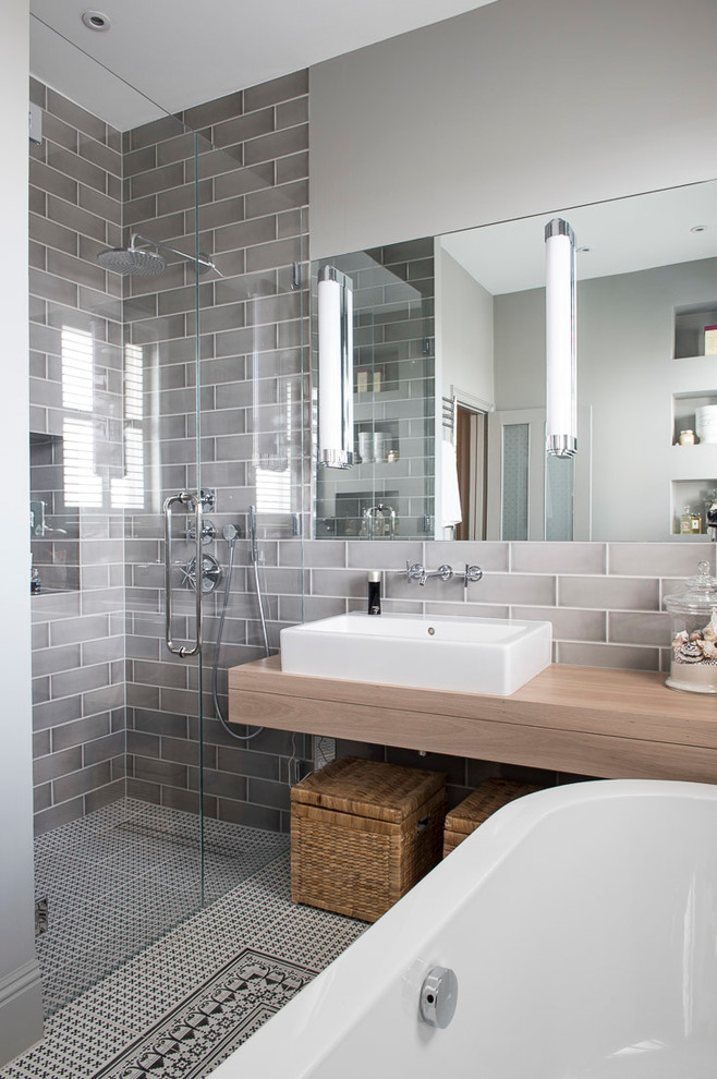 Design ideas for a transitional bathroom in London with a freestanding tub, an alcove shower, gray tile, subway tile, grey walls, a vessel sink, wood benchtops, a hinged shower door and beige benchtops.