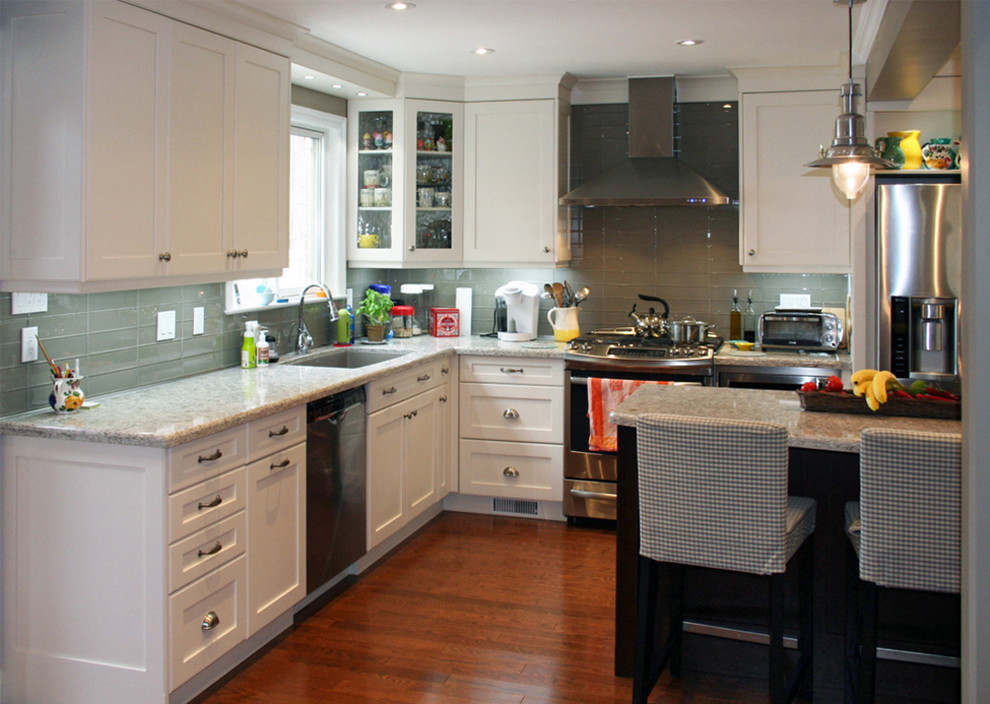 Inspiration for a large transitional l-shaped medium tone wood floor eat-in kitchen remodel in Toronto with an undermount sink, shaker cabinets, white cabinets, glass countertops, gray backsplash, glass tile backsplash, stainless steel appliances and an island