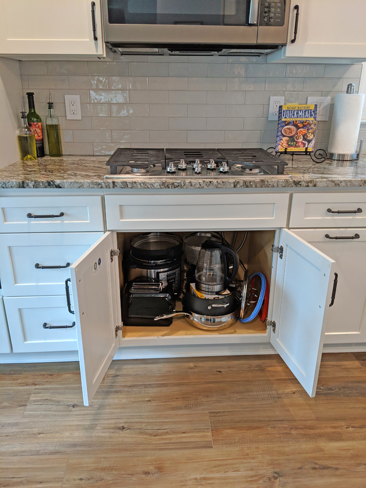 This is an example of a mid-sized transitional galley eat-in kitchen in Baltimore with a farmhouse sink, shaker cabinets, white cabinets, granite benchtops, grey splashback, subway tile splashback, stainless steel appliances, vinyl floors, with island, brown floor and multi-coloured benchtop.