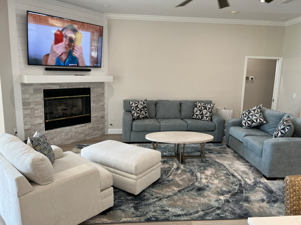 Expansive traditional open plan games room in Tampa with beige walls, laminate floors, a standard fireplace, a timber clad chimney breast, a wall mounted tv and grey floors.