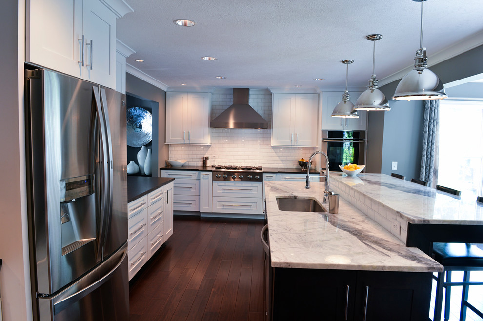 Inspiration for a transitional dark wood floor kitchen remodel in Cleveland with a drop-in sink, recessed-panel cabinets, white backsplash, ceramic backsplash, stainless steel appliances and an island