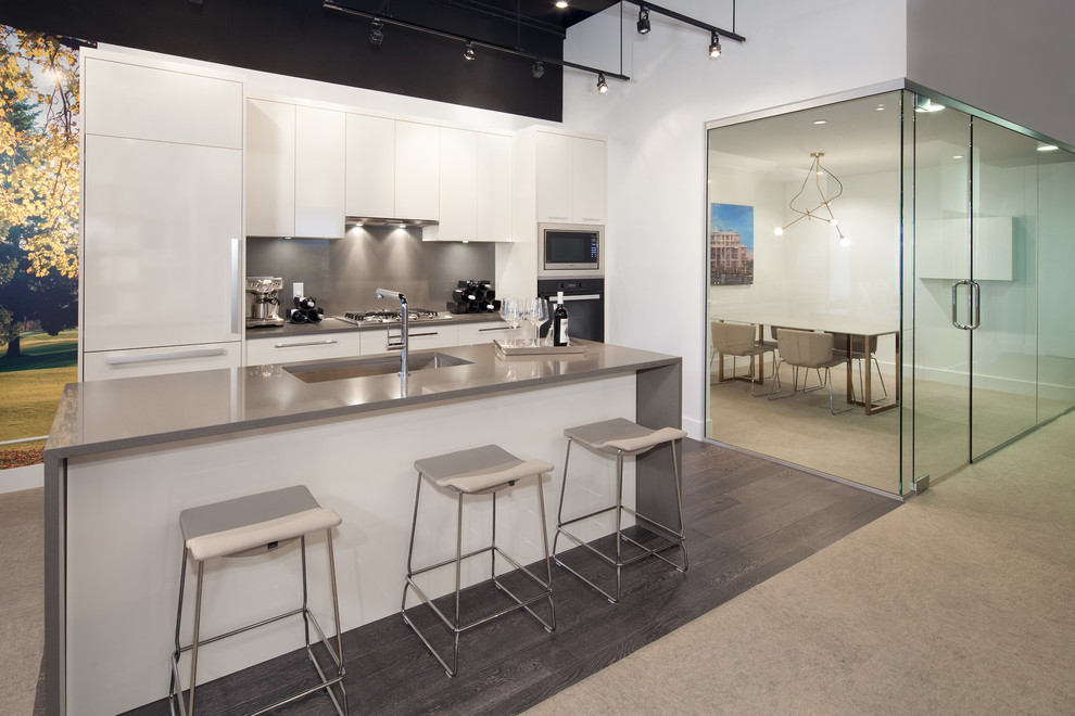 Small contemporary l-shaped open plan kitchen in Vancouver with an undermount sink, flat-panel cabinets, white cabinets, quartz benchtops, grey splashback, stainless steel appliances, dark hardwood floors and with island.