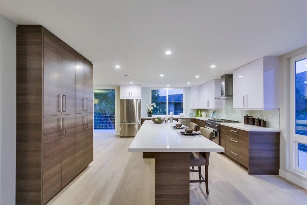 Photo of a large contemporary u-shaped eat-in kitchen in San Diego with flat-panel cabinets, grey cabinets, quartzite benchtops, white splashback, glass tile splashback, stainless steel appliances, light hardwood floors and with island.