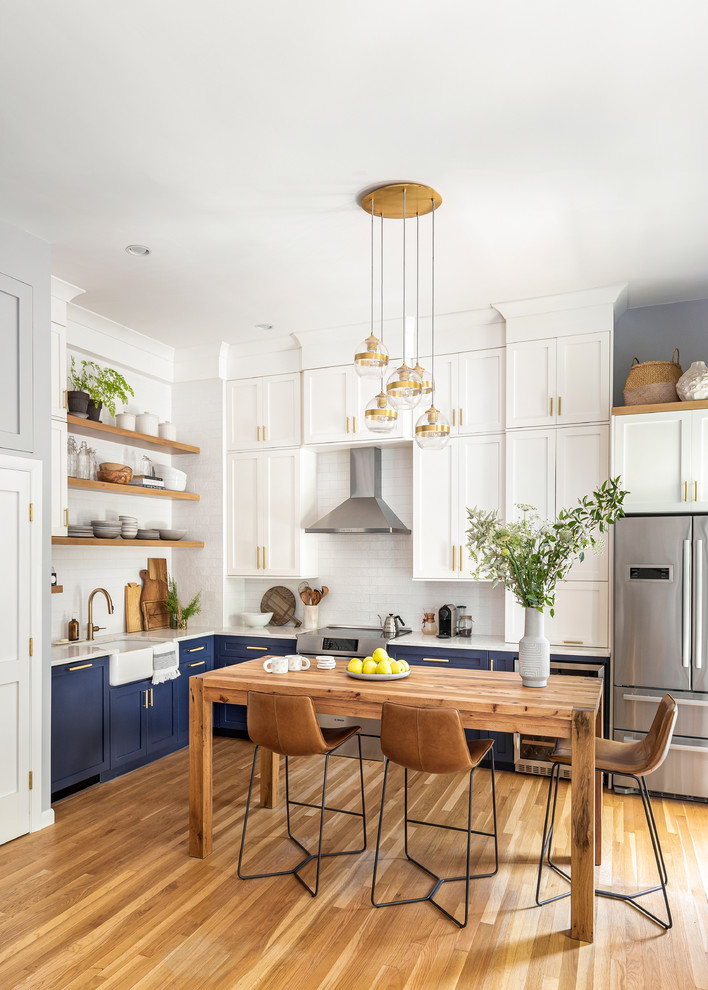 Transitional l-shaped eat-in kitchen in Boston with blue cabinets, white splashback, ceramic splashback, medium hardwood floors, a farmhouse sink, shaker cabinets, no island, brown floor and white benchtop.