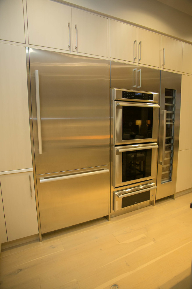 Inspiration for a mid-sized transitional l-shaped light wood floor kitchen remodel in New Orleans with an undermount sink, flat-panel cabinets, beige cabinets, multicolored backsplash, mosaic tile backsplash, stainless steel appliances and an island
