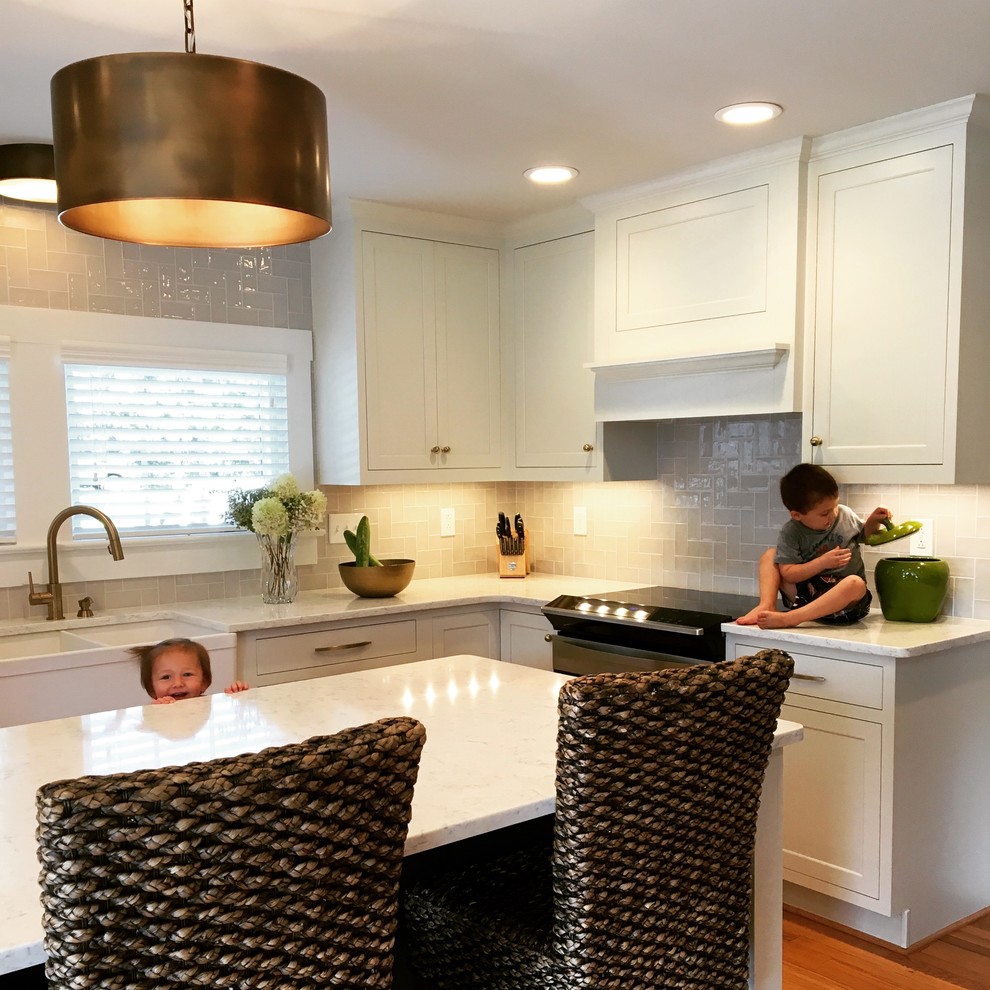 Open concept kitchen - mid-sized transitional u-shaped light wood floor and brown floor open concept kitchen idea with a farmhouse sink, recessed-panel cabinets, white cabinets, quartz countertops, beige backsplash, ceramic backsplash, stainless steel appliances and an island