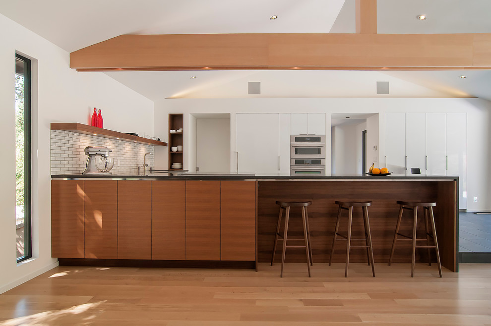 Photo of a contemporary kitchen in San Francisco with flat-panel cabinets, white cabinets, panelled appliances, white splashback and subway tile splashback.