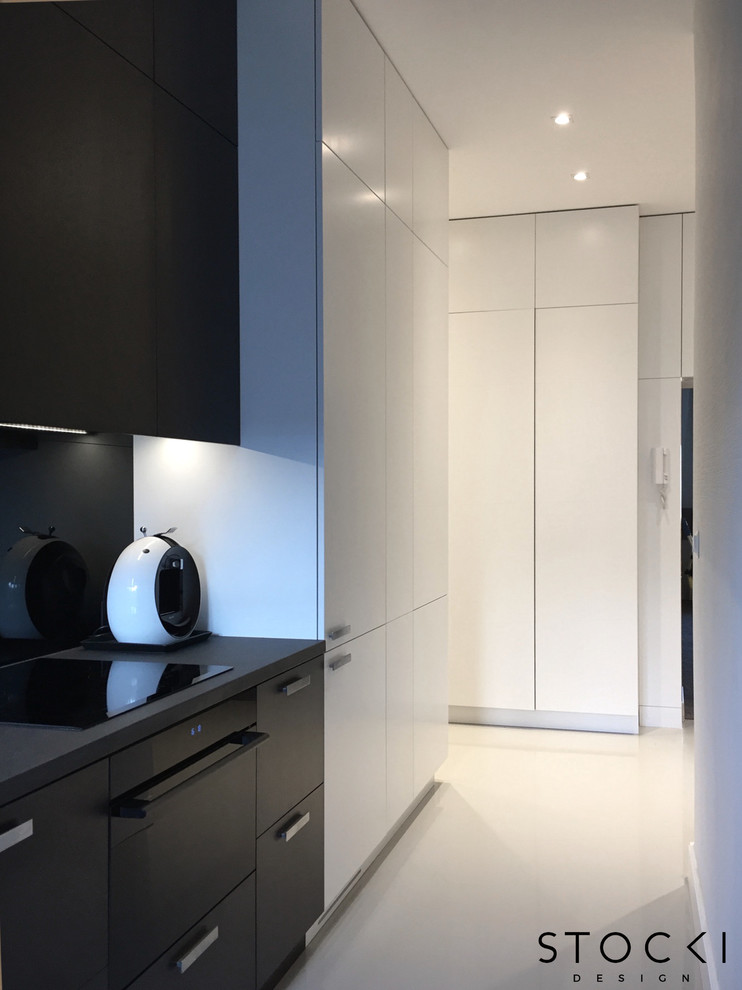 This is an example of a small modern galley separate kitchen in New York with white floor, an undermount sink, flat-panel cabinets, dark wood cabinets, granite benchtops, black splashback, glass sheet splashback, black appliances and no island.