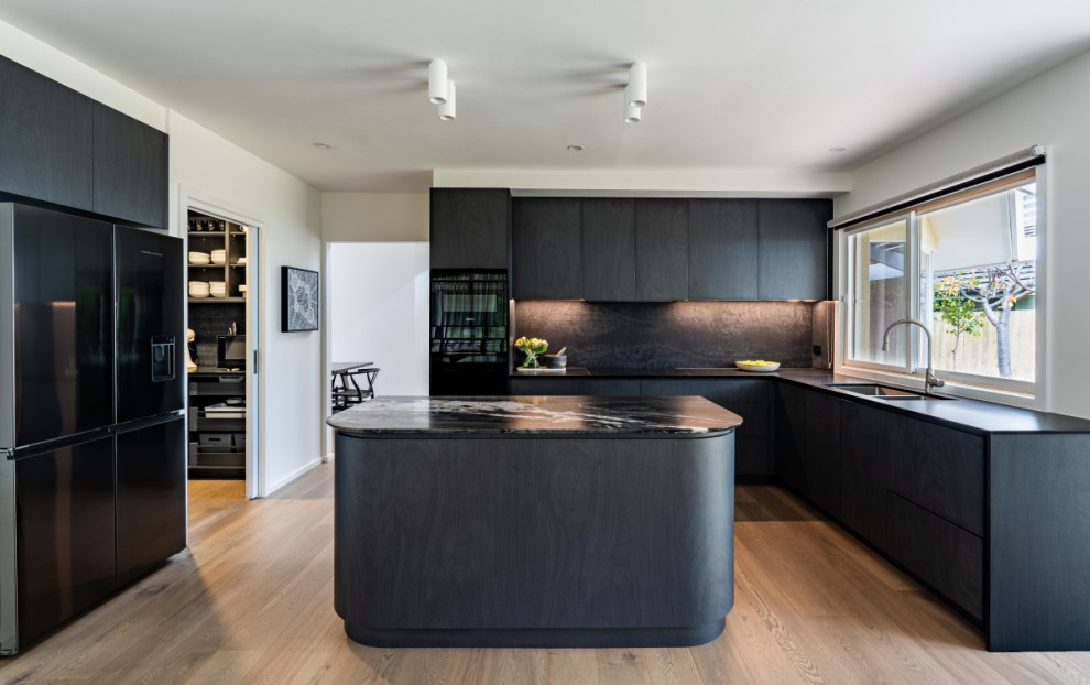 Photo of a mid-sized contemporary kitchen in Melbourne with marble benchtops, black splashback, engineered quartz splashback and black appliances.
