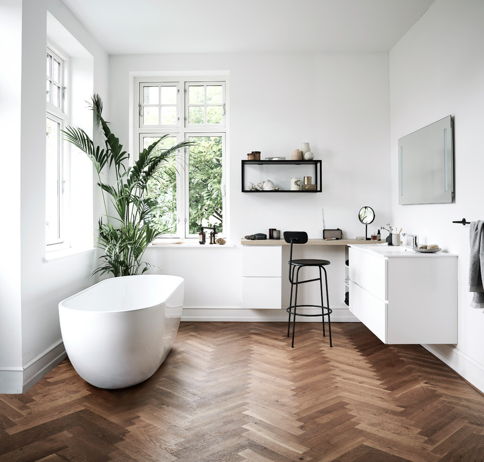 Photo of a large scandinavian master bathroom in Copenhagen with flat-panel cabinets, white cabinets, a freestanding tub, white walls, dark hardwood floors and brown floor.
