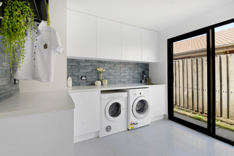 Photo of a contemporary l-shaped laundry room in Melbourne with flat-panel cabinets, white cabinets, grey floor and grey benchtop.
