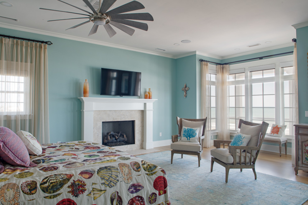 広いビーチスタイルのおしゃれな主寝室 (青い壁、標準型暖炉、石材の暖炉まわり、茶色い床、淡色無垢フローリング) のインテリア