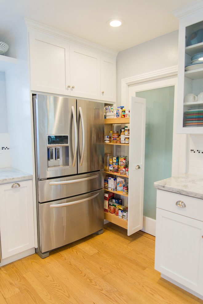 Photo of a mid-sized eclectic u-shaped separate kitchen in Sacramento with a single-bowl sink, shaker cabinets, white cabinets, marble benchtops, white splashback, ceramic splashback, stainless steel appliances, light hardwood floors and a peninsula.