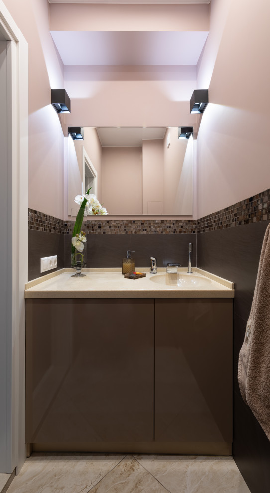 Пример оригинального дизайна: туалет среднего размера в стиле неоклассика (современная классика) с плоскими фасадами, бежевыми фасадами, инсталляцией, коричневой плиткой, керамической плиткой, коричневыми стенами, полом из керамогранита, монолитной раковиной, столешницей из искусственного камня, коричневым полом, бежевой столешницей, встроенной тумбой и балками на потолке