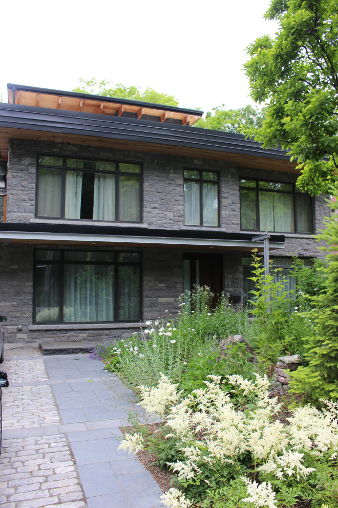 Photo of a large midcentury three-storey grey house exterior in Toronto with stone veneer, a flat roof and a green roof.
