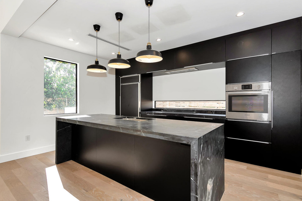 Photo of a contemporary galley kitchen/diner in Miami with flat-panel cabinets, black cabinets, marble worktops, laminate floors, an island, brown floors and black worktops.