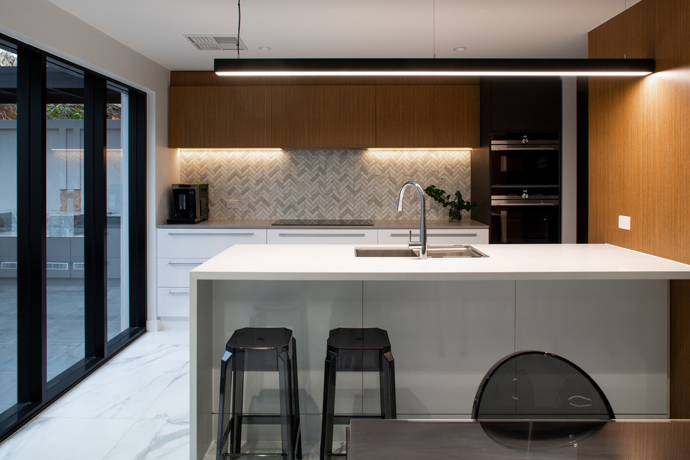 Photo of a mid-sized contemporary kitchen in Adelaide with brown cabinets, solid surface benchtops, grey splashback, ceramic splashback, black appliances, marble floors, with island, grey floor and white benchtop.