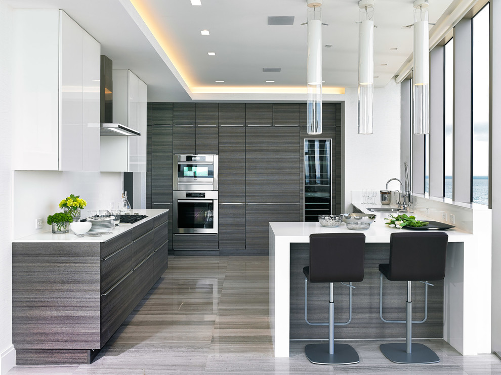 Large contemporary u-shaped separate kitchen in Miami with an undermount sink, flat-panel cabinets, stainless steel appliances, a peninsula, grey cabinets, solid surface benchtops, white splashback, ceramic floors and white benchtop.