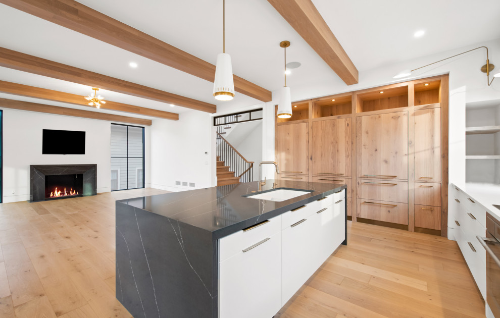 This is an example of a large transitional u-shaped open plan kitchen in Chicago with an undermount sink, flat-panel cabinets, white cabinets, quartz benchtops, white splashback, porcelain splashback, coloured appliances, light hardwood floors, with island, brown floor and black benchtop.
