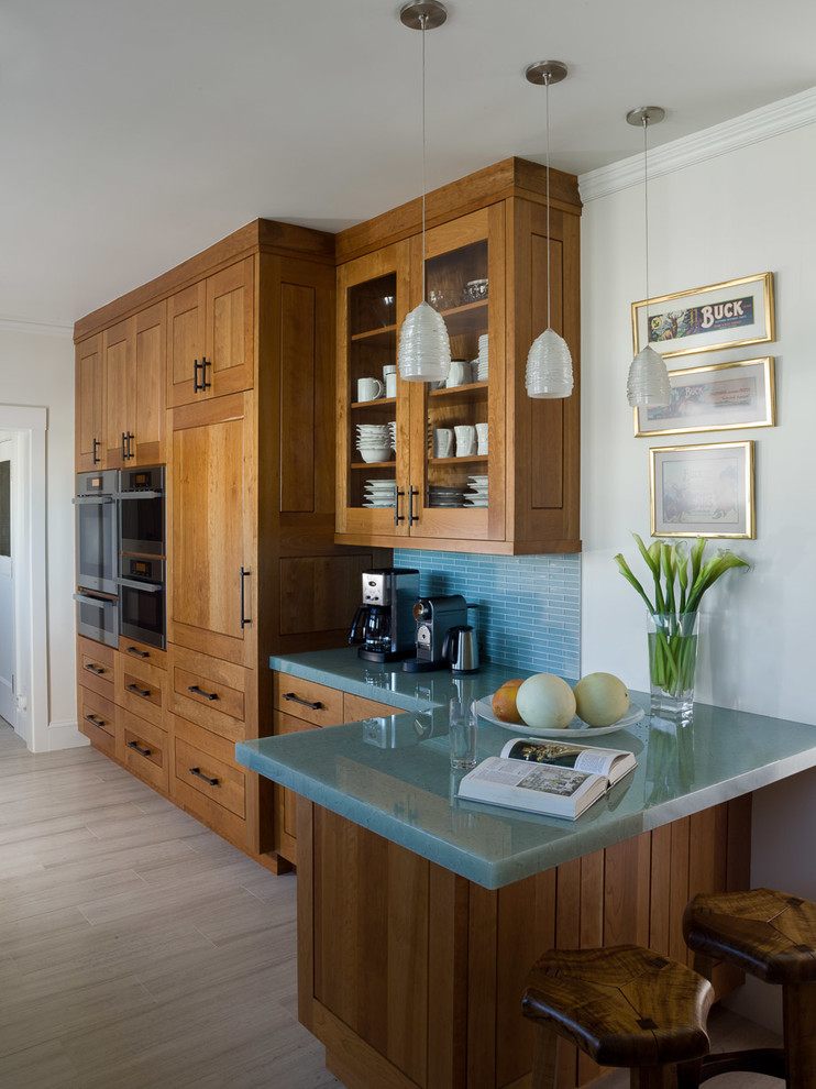 This is an example of a mid-sized contemporary galley separate kitchen in San Francisco with a double-bowl sink, shaker cabinets, medium wood cabinets, glass benchtops, blue splashback, matchstick tile splashback, stainless steel appliances, porcelain floors, a peninsula and turquoise benchtop.