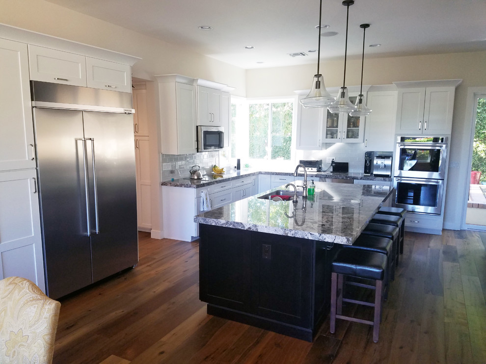 Large transitional l-shaped medium tone wood floor eat-in kitchen photo in Phoenix with an undermount sink, shaker cabinets, white cabinets, granite countertops, gray backsplash, subway tile backsplash, stainless steel appliances and an island