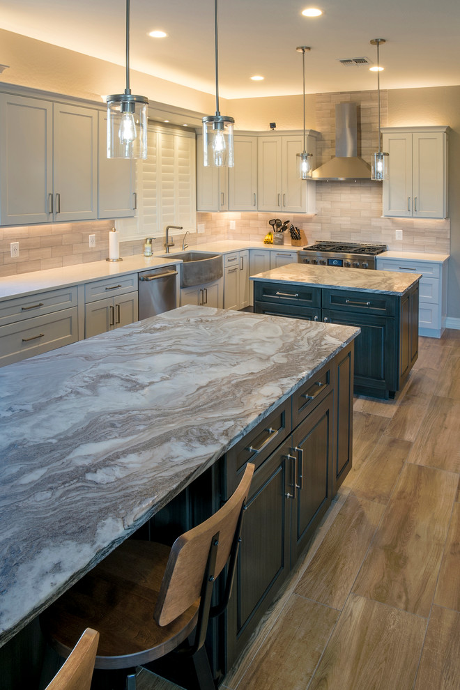 Huge transitional l-shaped porcelain tile and brown floor eat-in kitchen photo in Phoenix with a farmhouse sink, recessed-panel cabinets, white cabinets, quartz countertops, gray backsplash, stone tile backsplash, stainless steel appliances and two islands