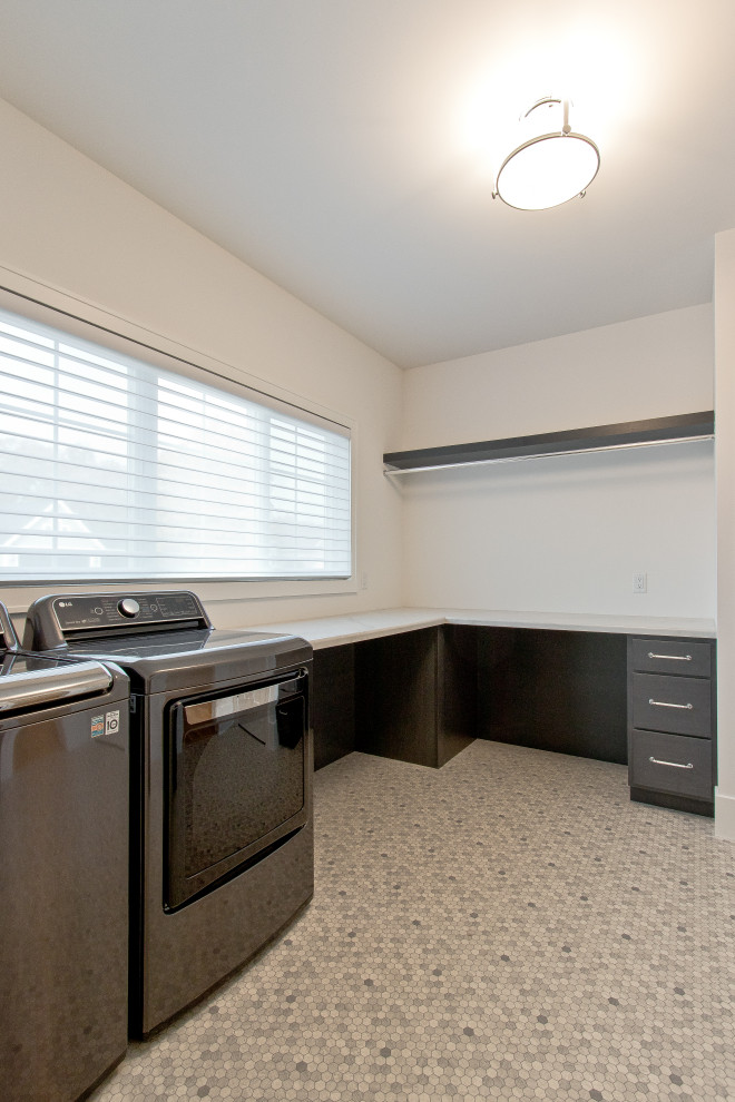 Design ideas for a transitional l-shaped dedicated laundry room in Other with flat-panel cabinets, black cabinets, quartz benchtops, white walls, vinyl floors, a side-by-side washer and dryer, multi-coloured floor and white benchtop.